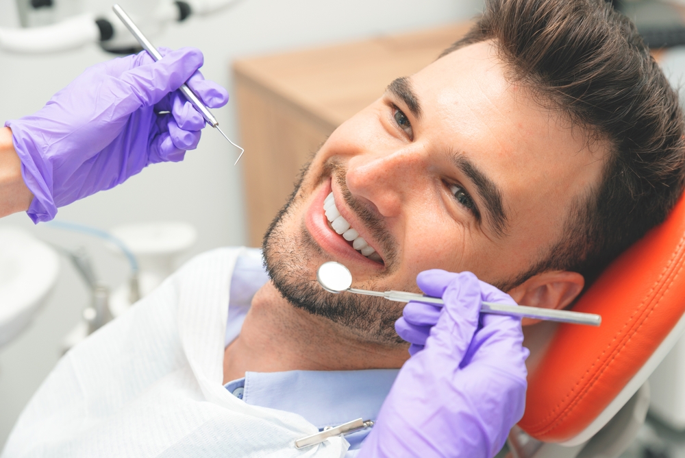 Man smiling while dentist prepare to examine mouth during preventive visit.