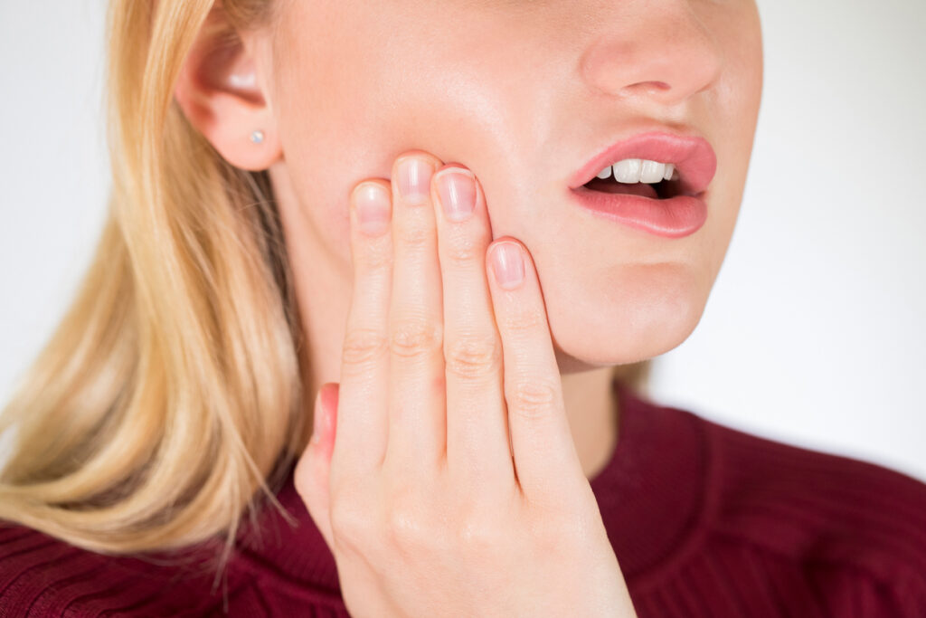 Person holding their jaw in discomfort, representing stress-related TMJ pain and jaw tension.